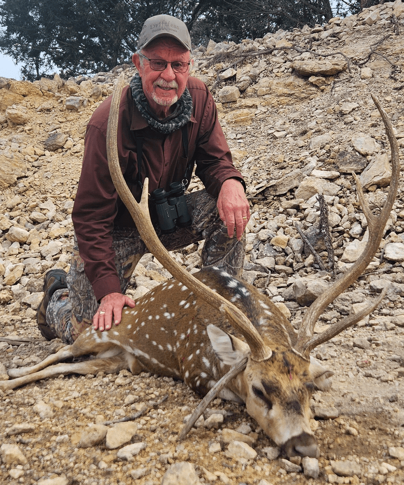 Hunter with an Axis buck on a rocky slope