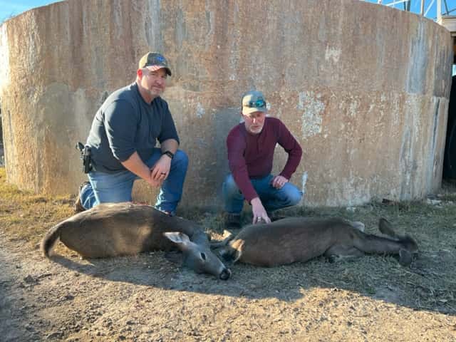Two hunters with two deer in front of a round tank
