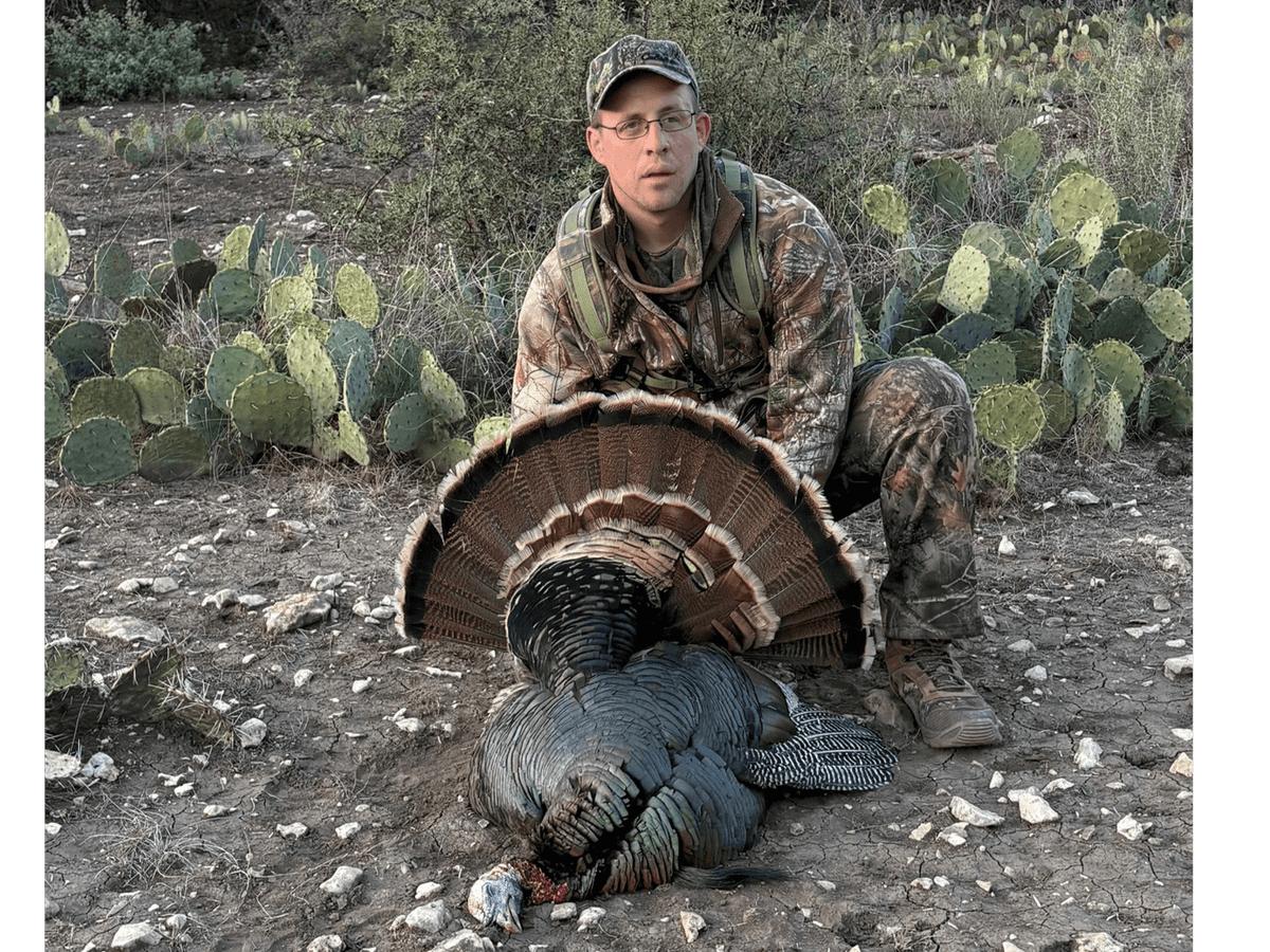 Hunter displaying a turkey's fanned tail beside cactus
