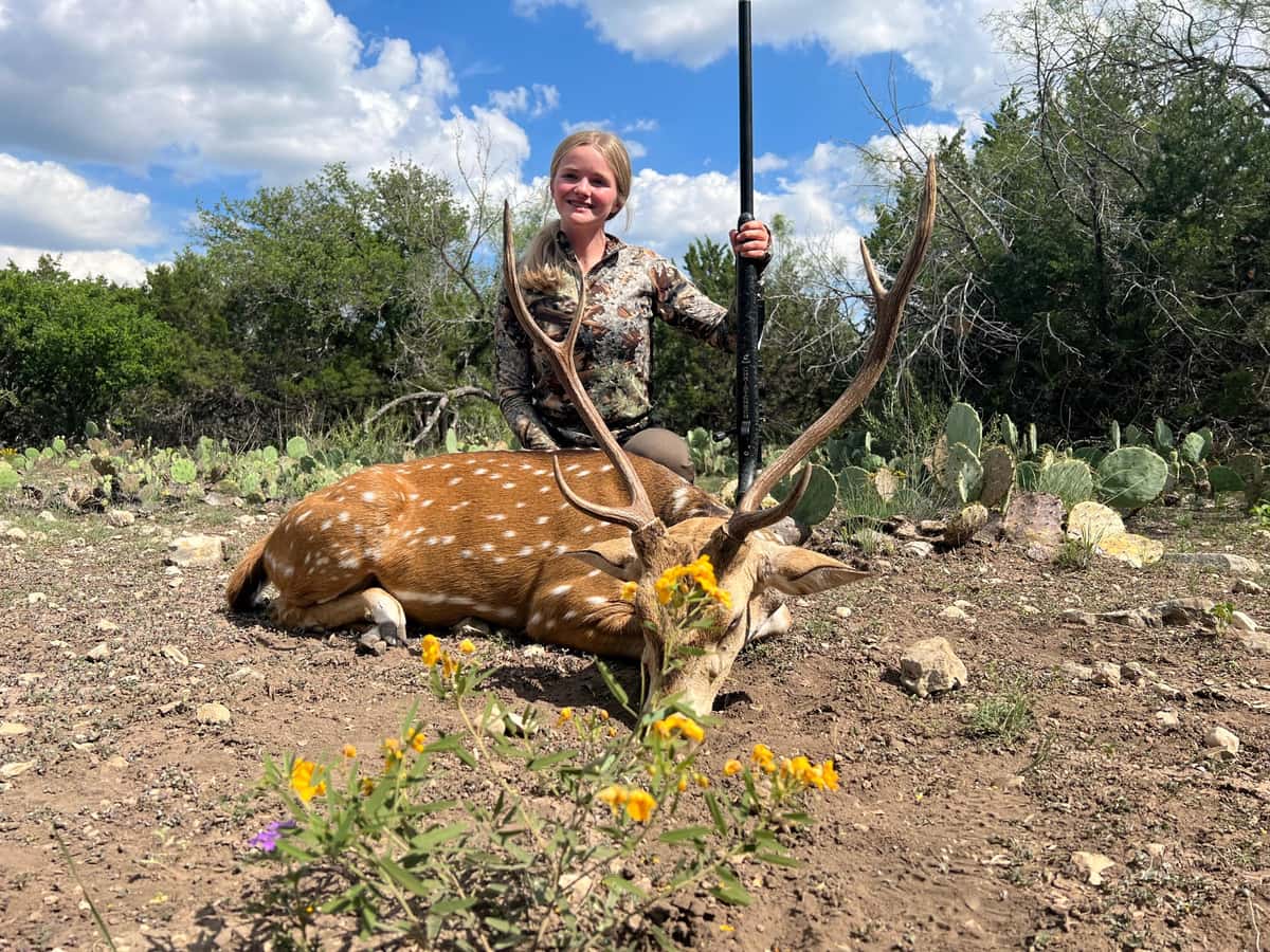 Hunter with an Axis buck beside wildflowers and cactus
