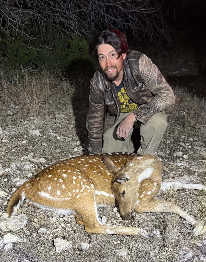 Hunter kneeling beside an Axis deer at night