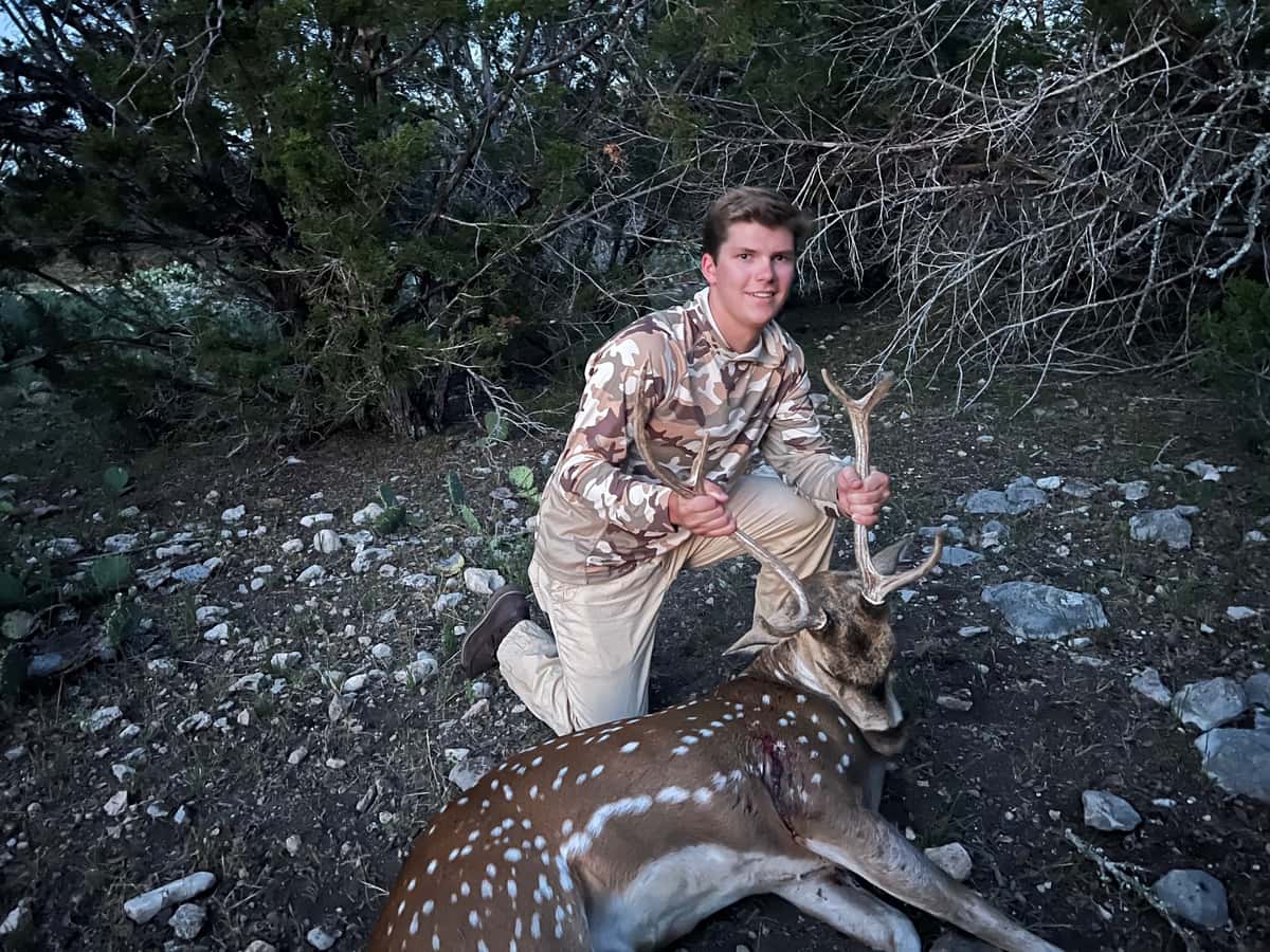 Hunter kneeling with an Axis buck on rocky ground