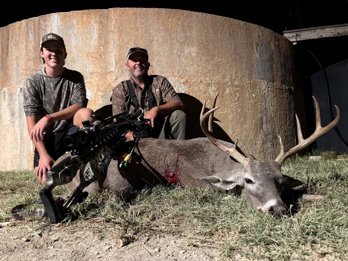 Two hunters with whitetail bucks beside a round tank