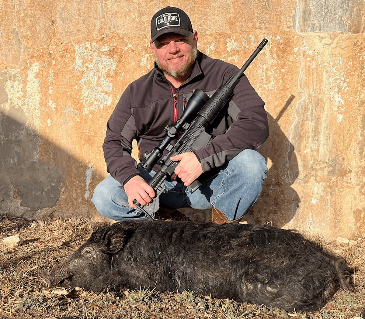 Hunter with a harvested hog beside a round tank