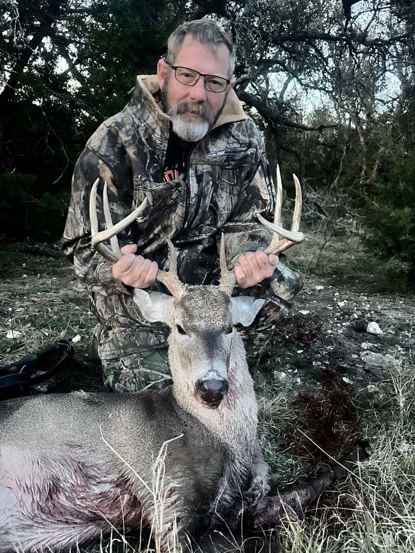 Hunter holding a whitetail buck's antlers beneath a tree