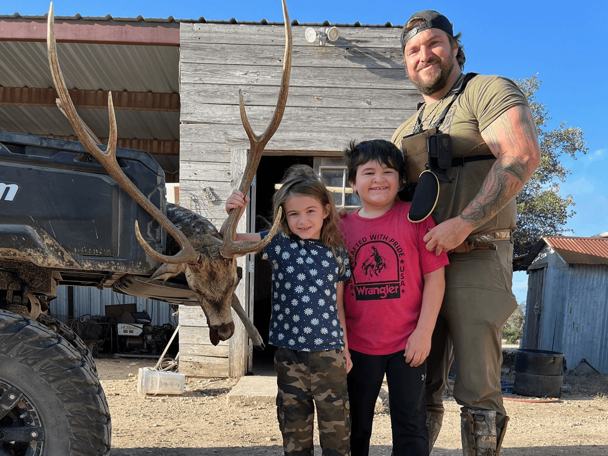 Hunter and two children posing beside Axis antlers at a ranch building