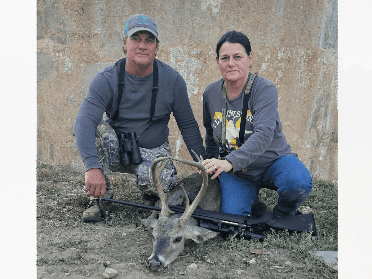 Two hunters with a whitetail buck beside a round tank