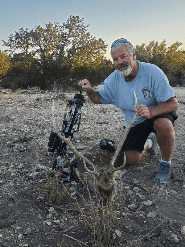 Bow hunter with an Axis buck in a clearing