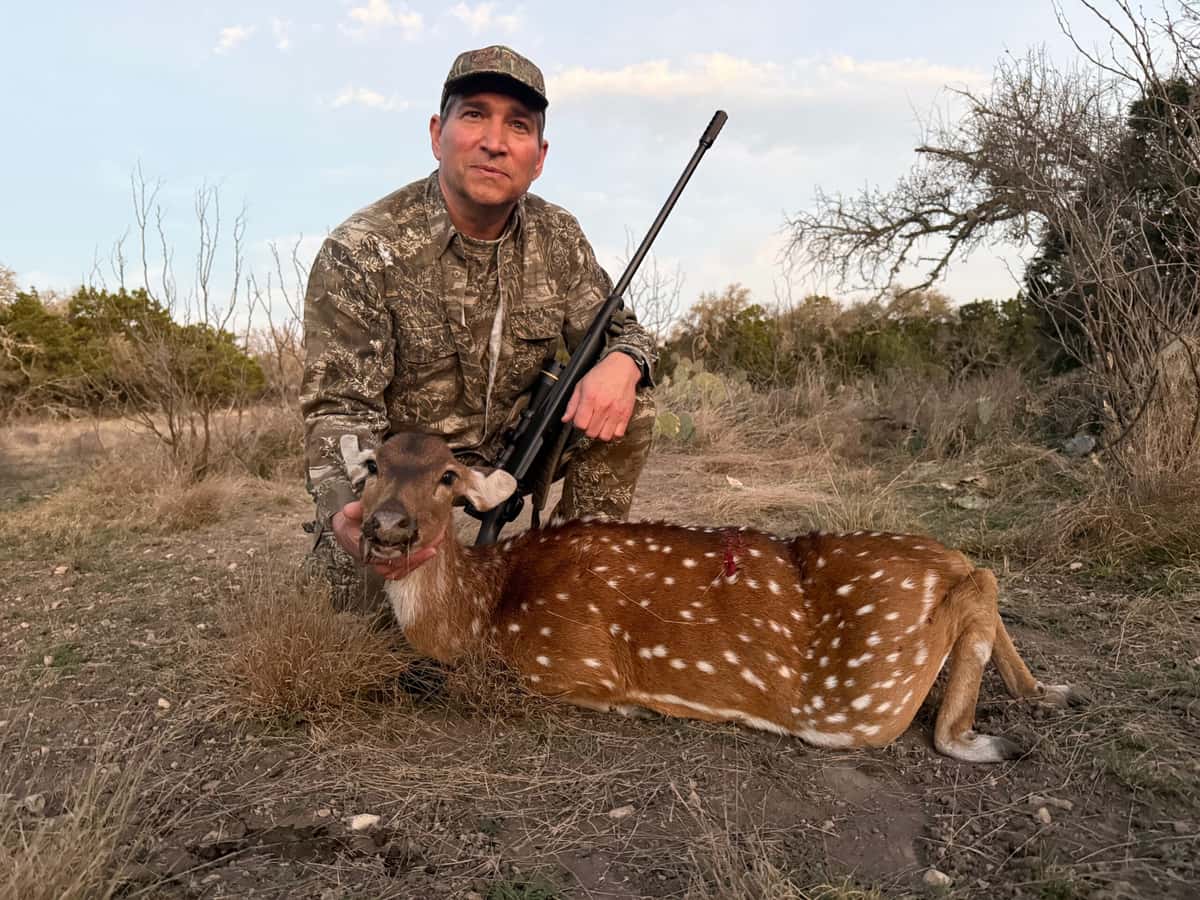 Hunter with an Axis deer in dry grass