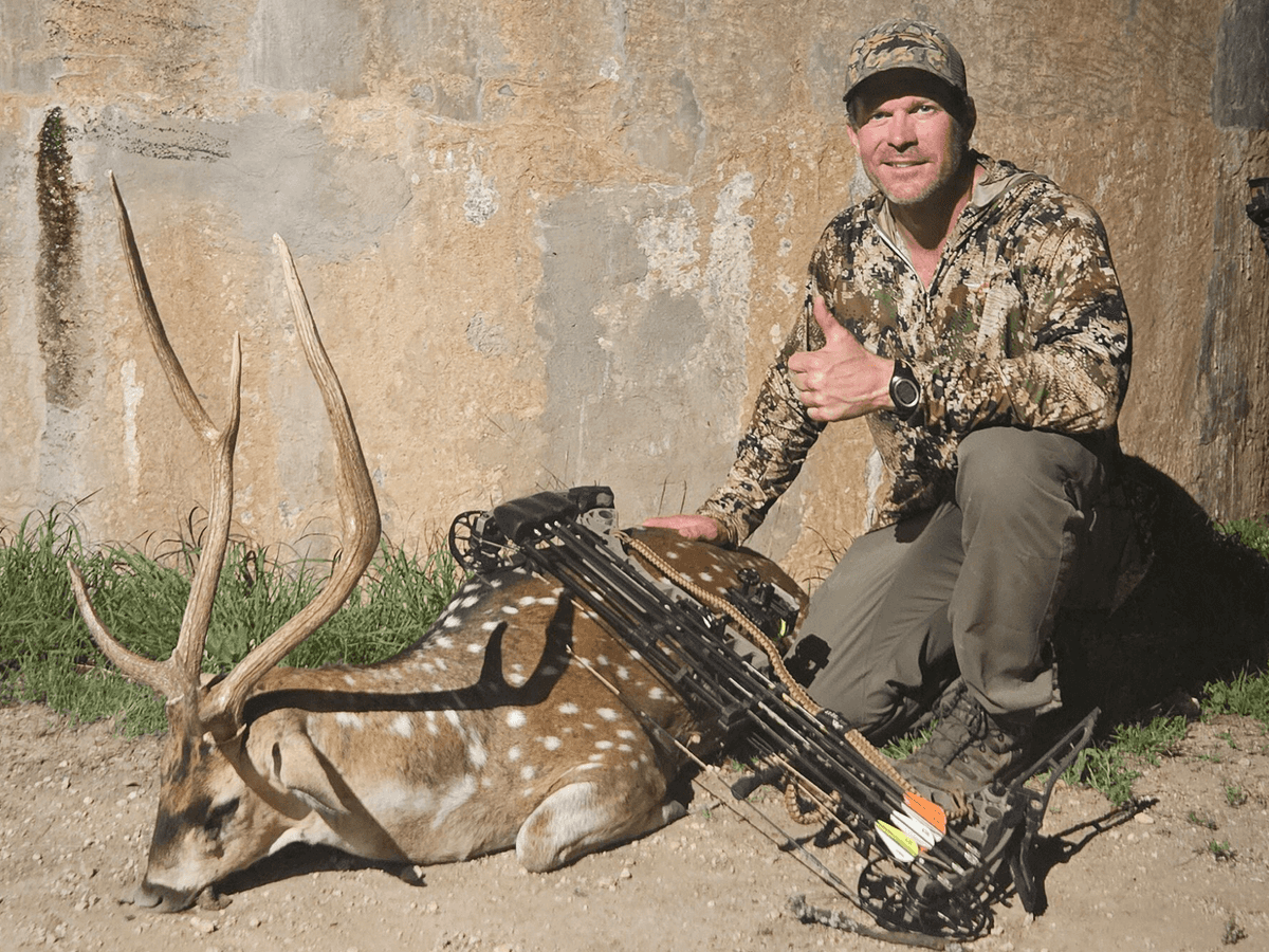 Bow hunter with an Axis buck beside a round tank