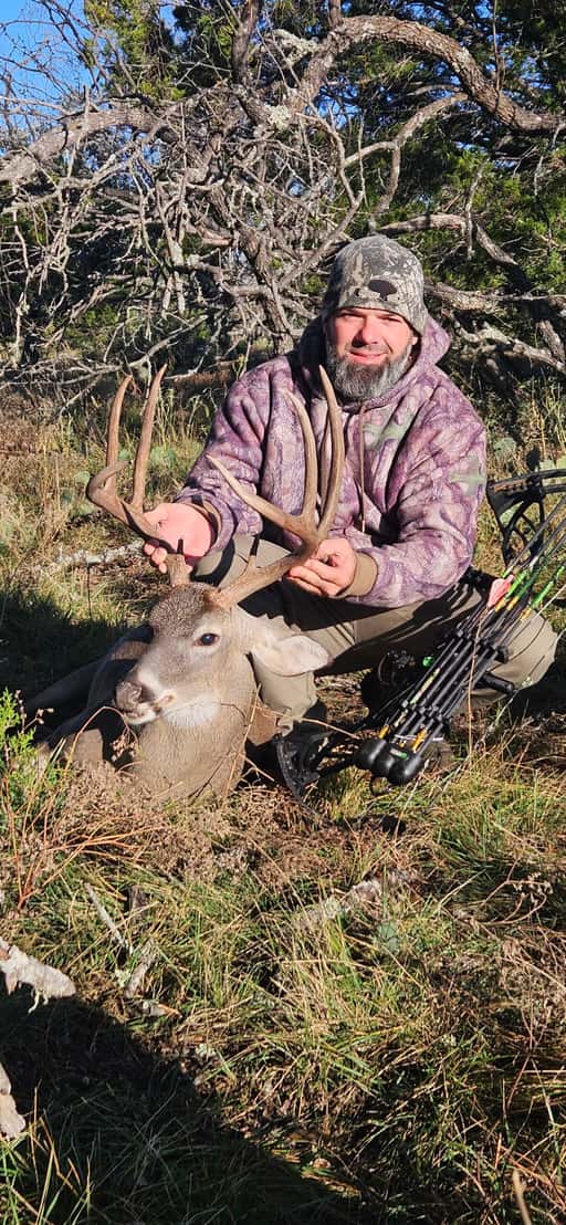Bow hunter with a whitetail buck beside cedar trees