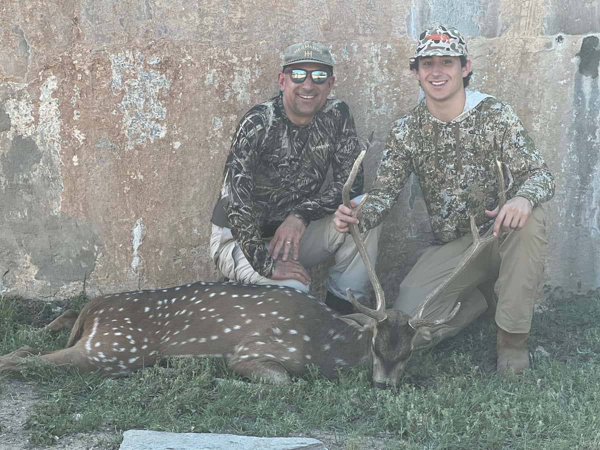 Two hunters with an Axis buck beside a round tank