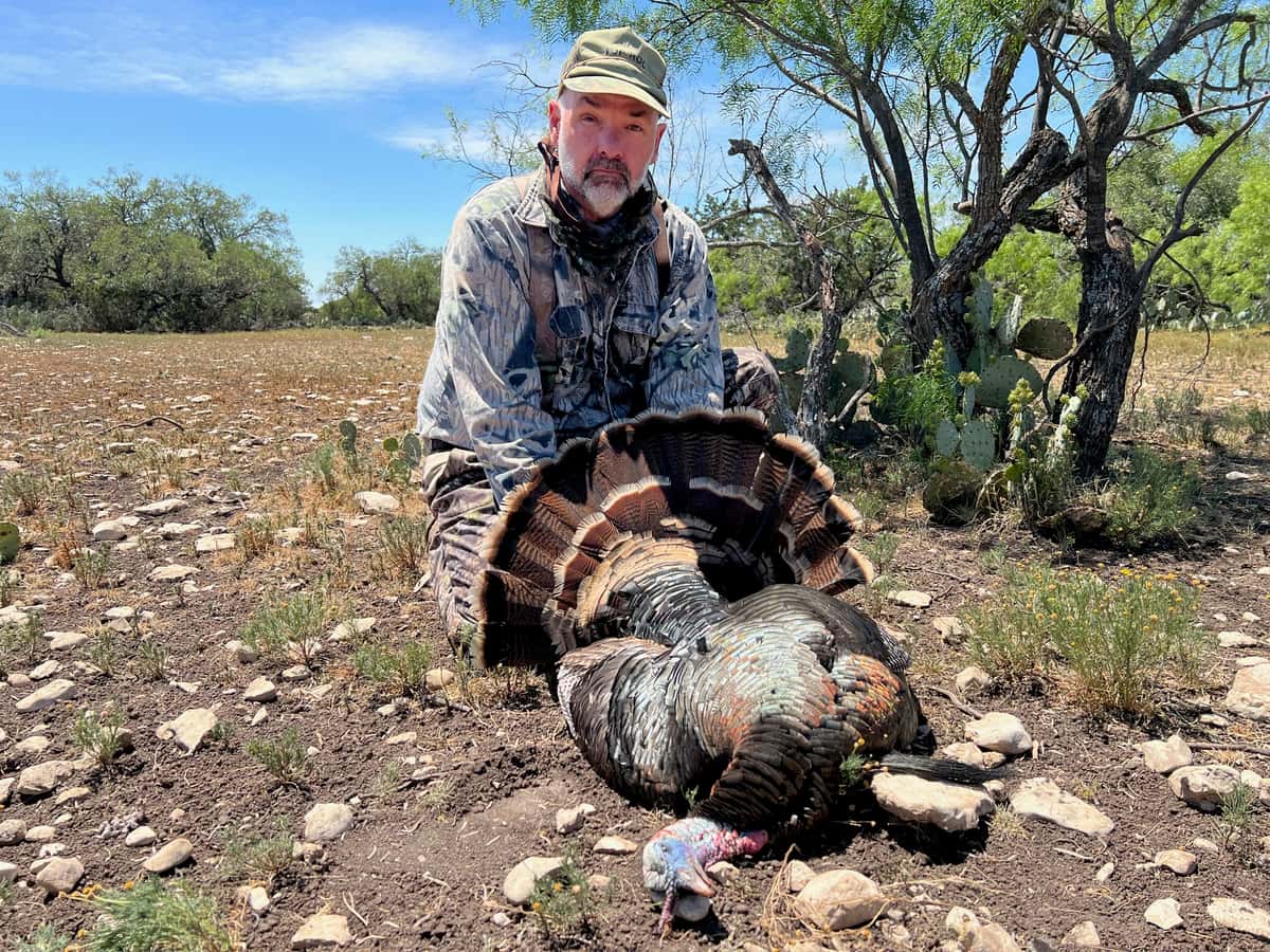 Hunter with a turkey beneath a tree