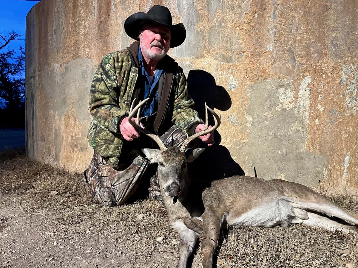 Hunter in a black hat with a whitetail buck beside a tank