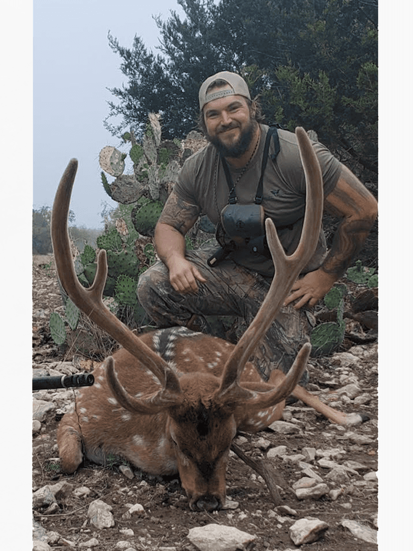 Hunter holding an Axis buck's antlers on rocky ground