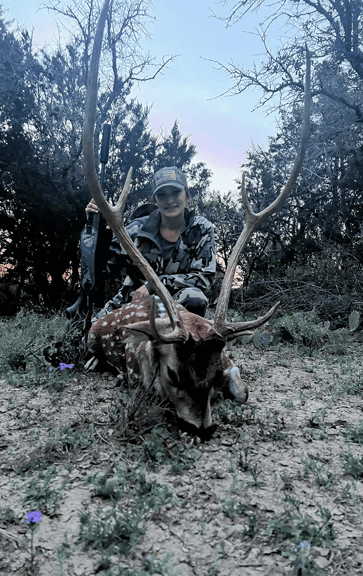 Hunter with an Axis buck beneath trees