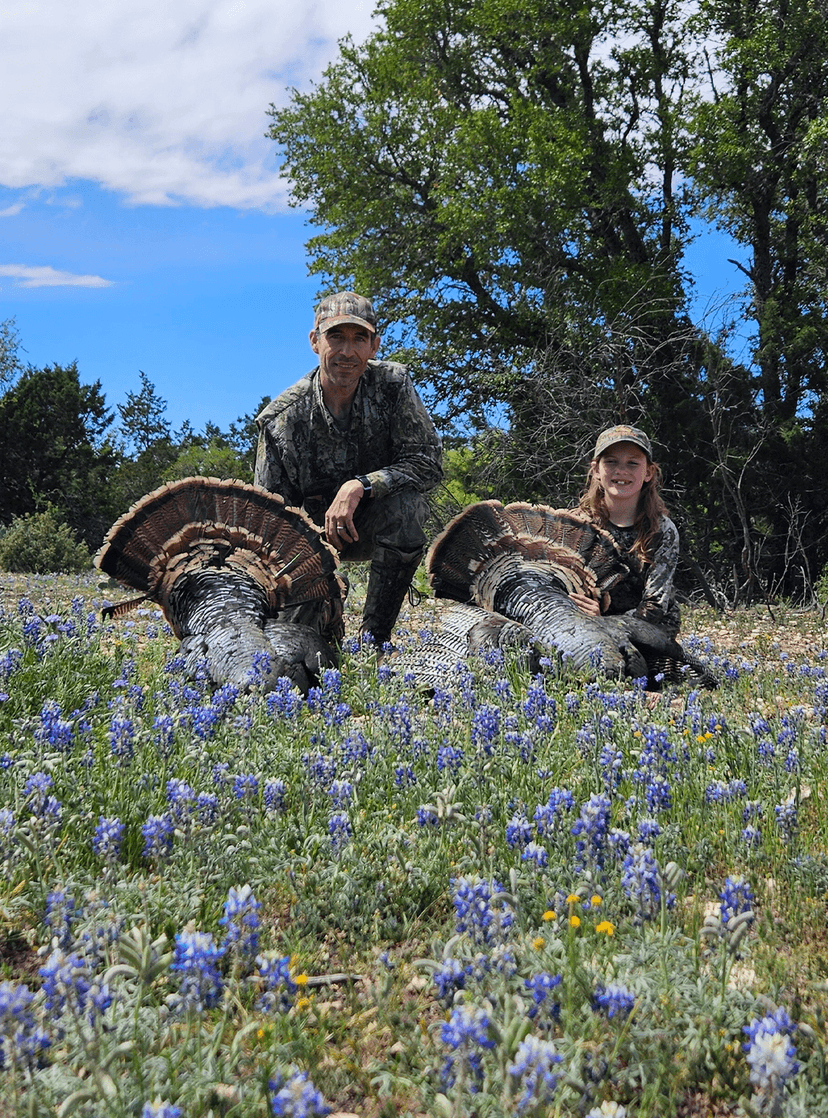 Two hunters with turkeys among bluebonnets