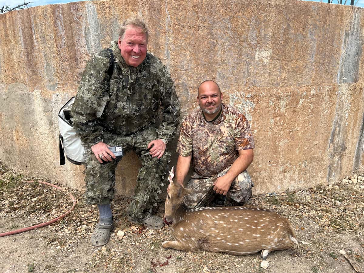 Two hunters with an Axis deer beside a round tank