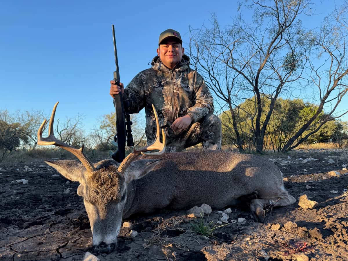 Hunter with a rifle and whitetail buck beneath a blue sky