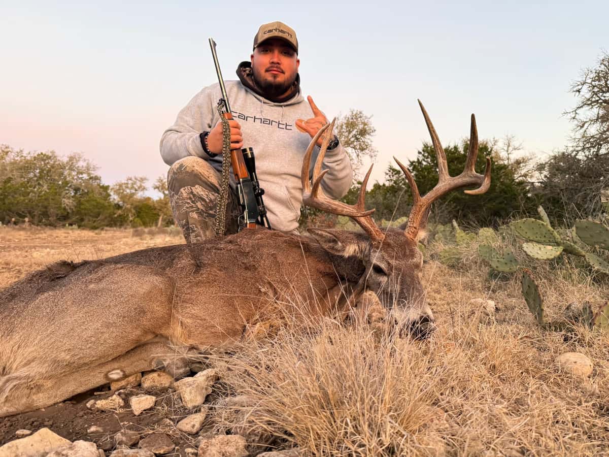Hunter with a whitetail buck in dry grass and cactus