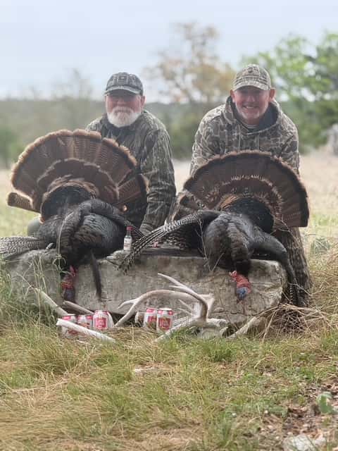 Two hunters displaying turkeys in a grassy clearing