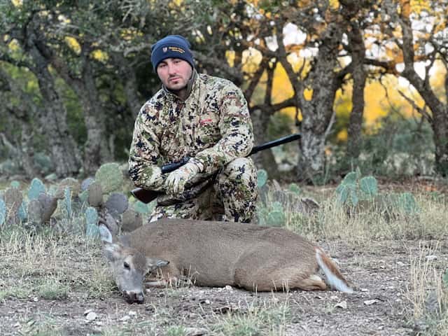 Hunter with a whitetail buck beside cactus and trees