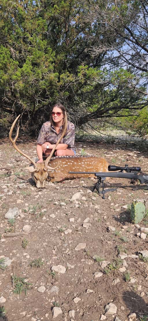 Hunter with a harvested axis buck in rocky cedar terrain at FF Hunting Ranch