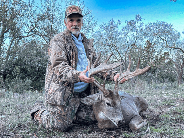 Hunter kneeling with a whitetail buck in dry grass