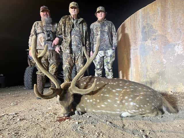 Three hunters with an Axis buck beside a round tank at night