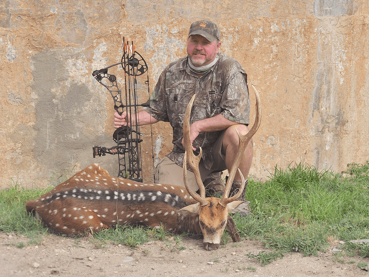 Bow hunter with an Axis buck in front of a round tank