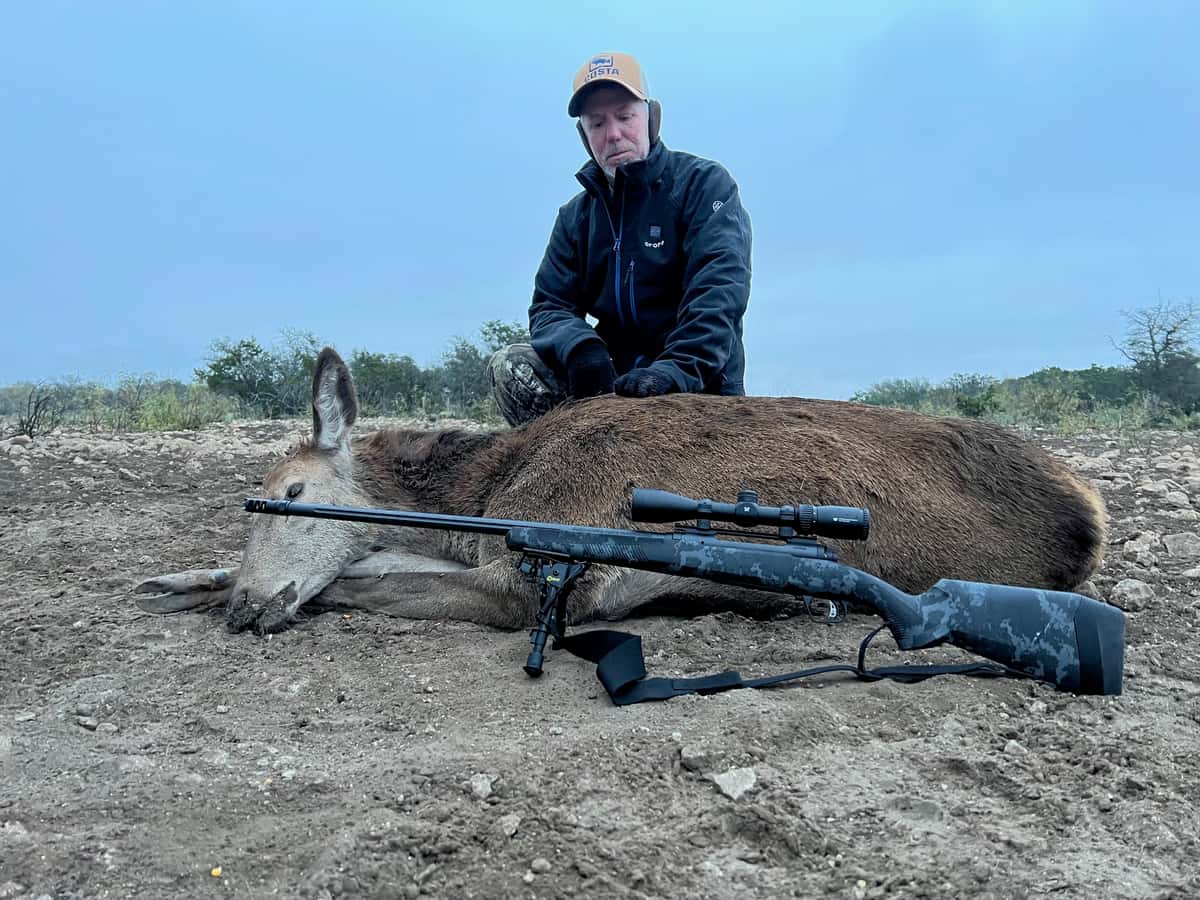Hunter with a harvested hog and rifle in a clearing