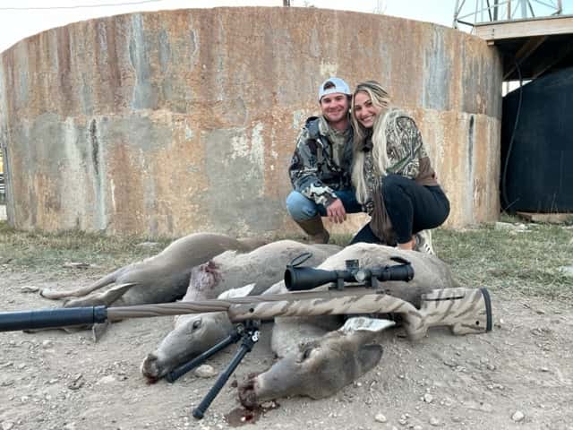 Two people posing behind harvested deer beside a round tank