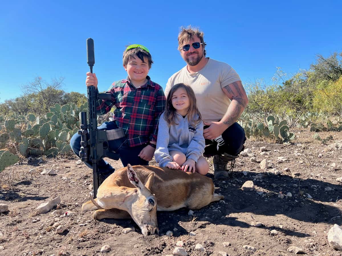 Three hunters with a harvested hog beside cactus