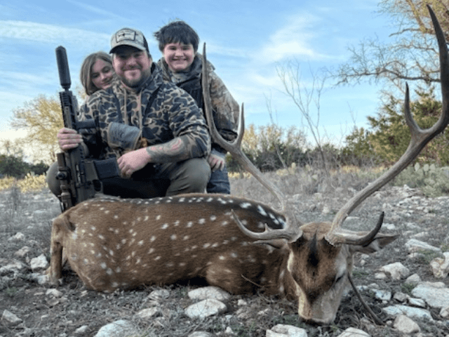 Three hunters with an Axis buck in a rocky clearing