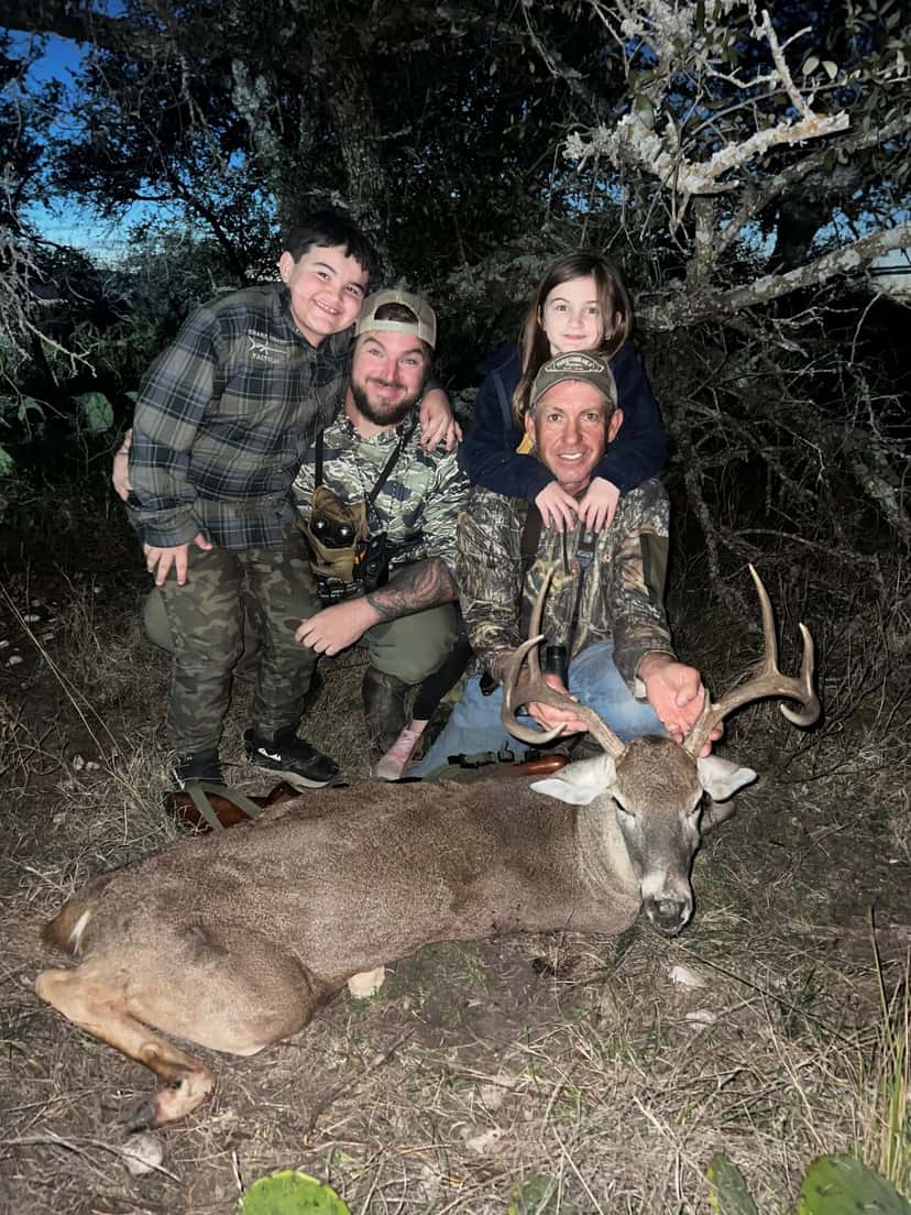 Group posing with a whitetail buck beside cedar trees