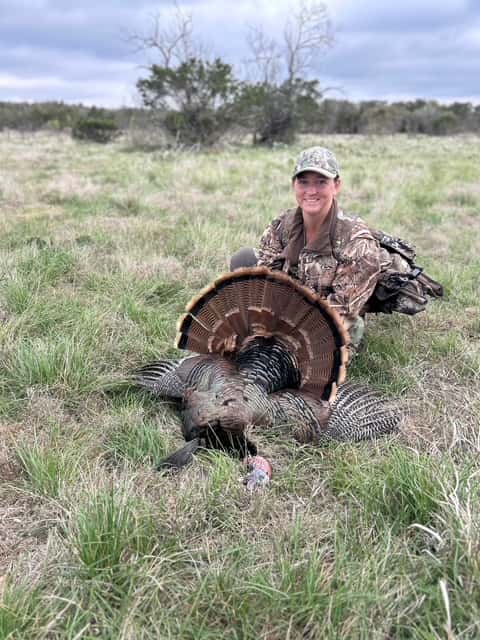 Hunter with a turkey in green grass