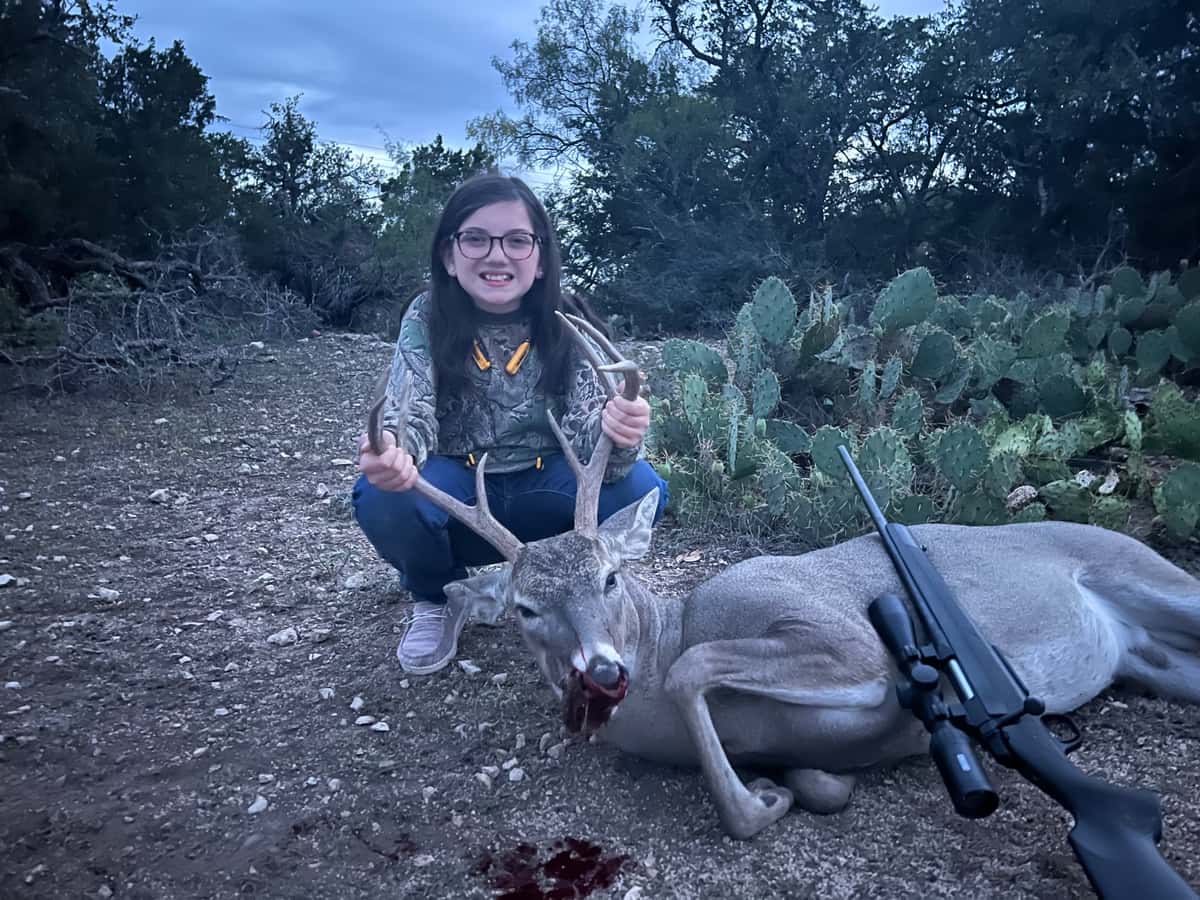 Hunter with a whitetail buck and rifle beside cactus