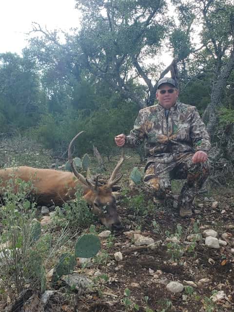 Hunter with an antlered deer beside cactus