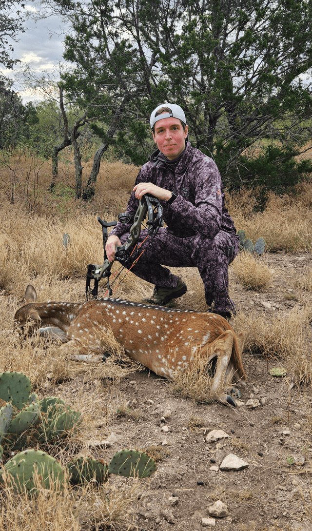 Bow hunter with an Axis doe in dry grass