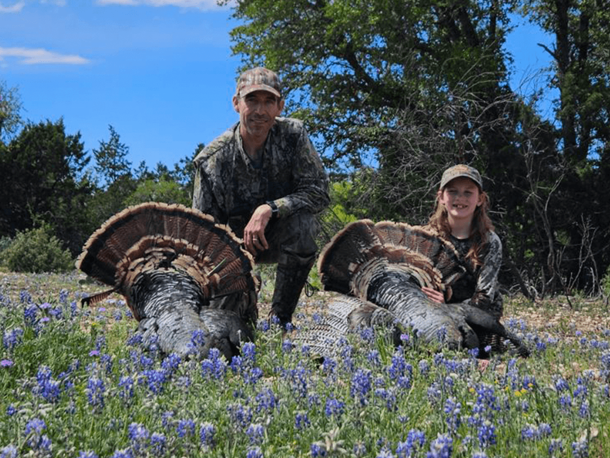 Two hunters displaying turkeys among bluebonnets