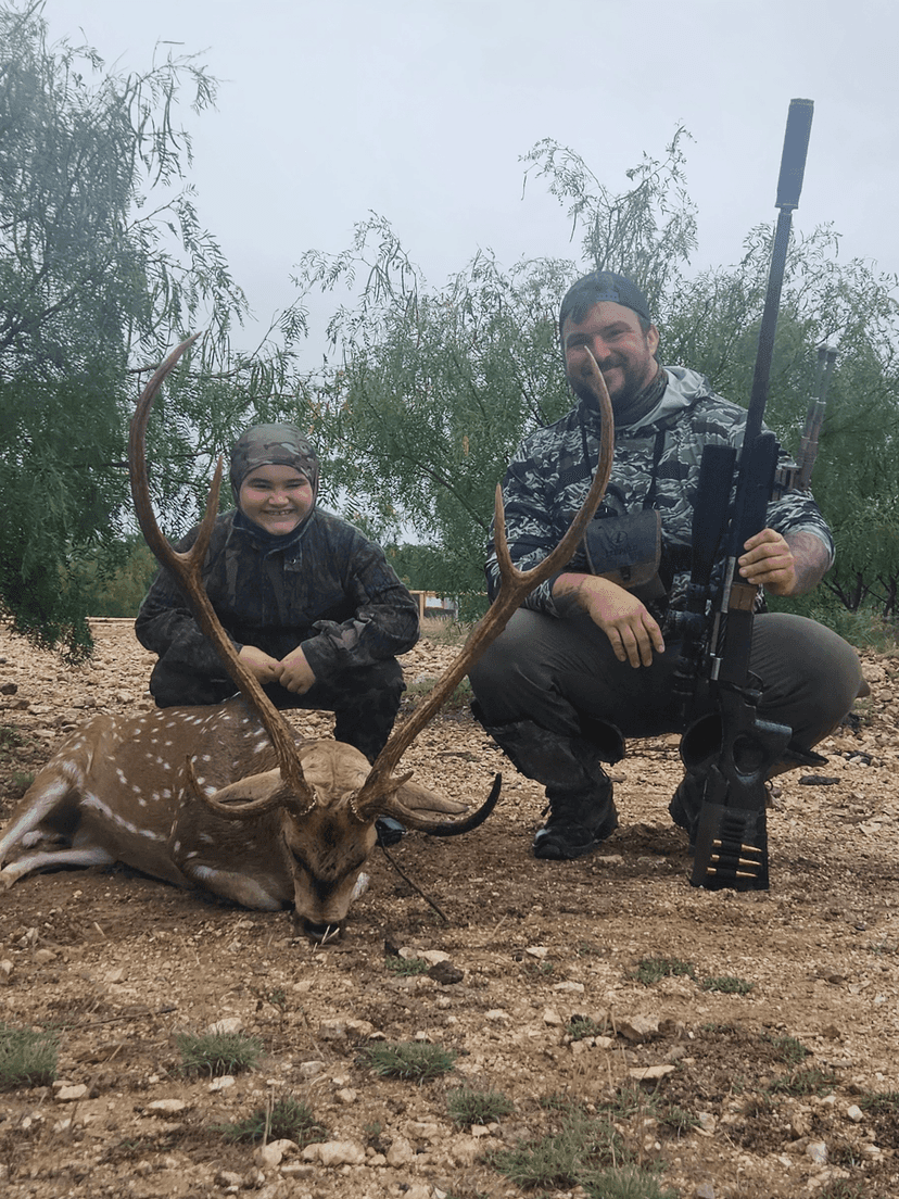 Two hunters with an Axis buck on rocky ground