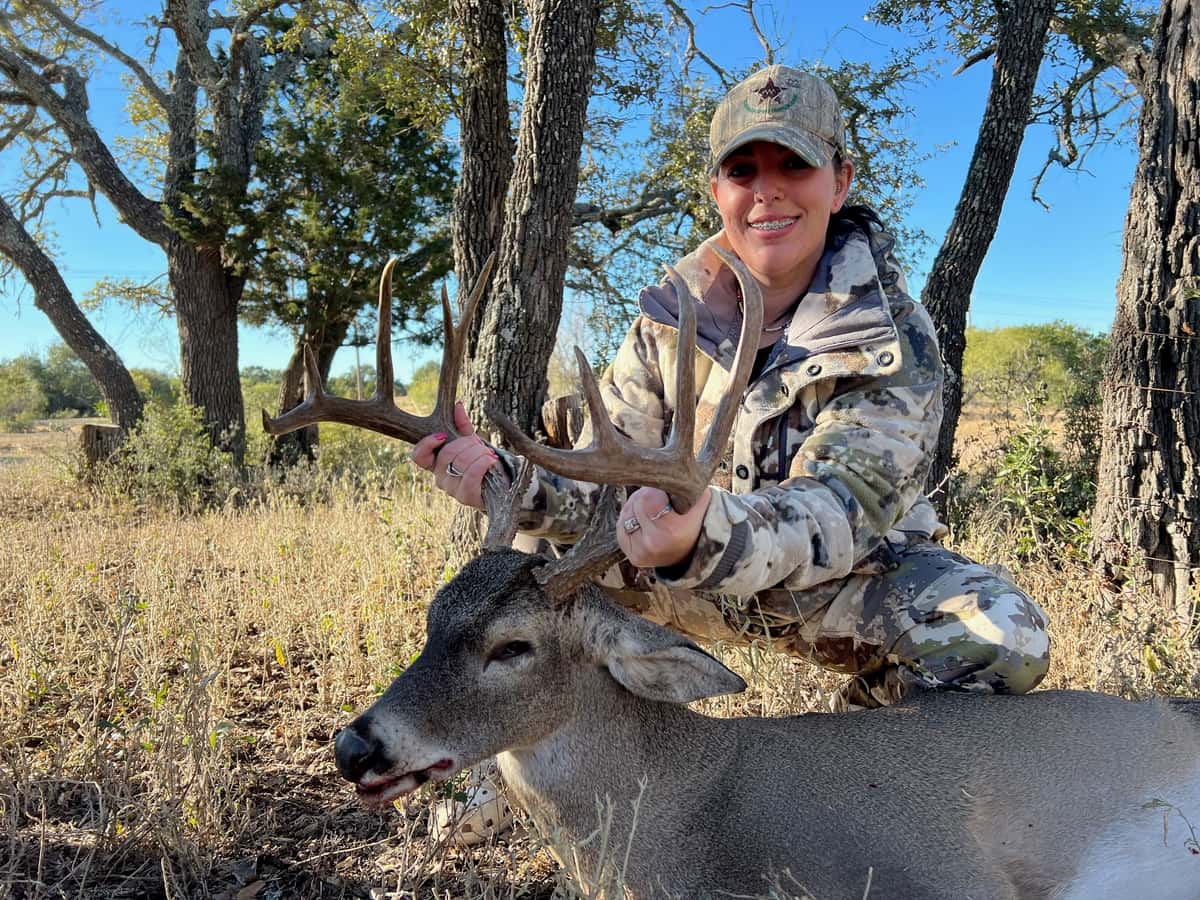 Hunter holding a whitetail buck's antlers beneath a tree