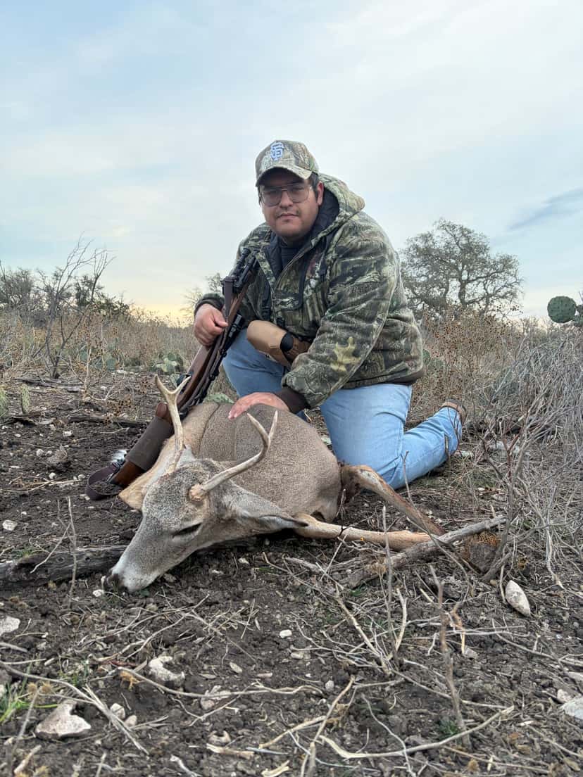 Hunter kneeling behind a whitetail buck on rocky ground