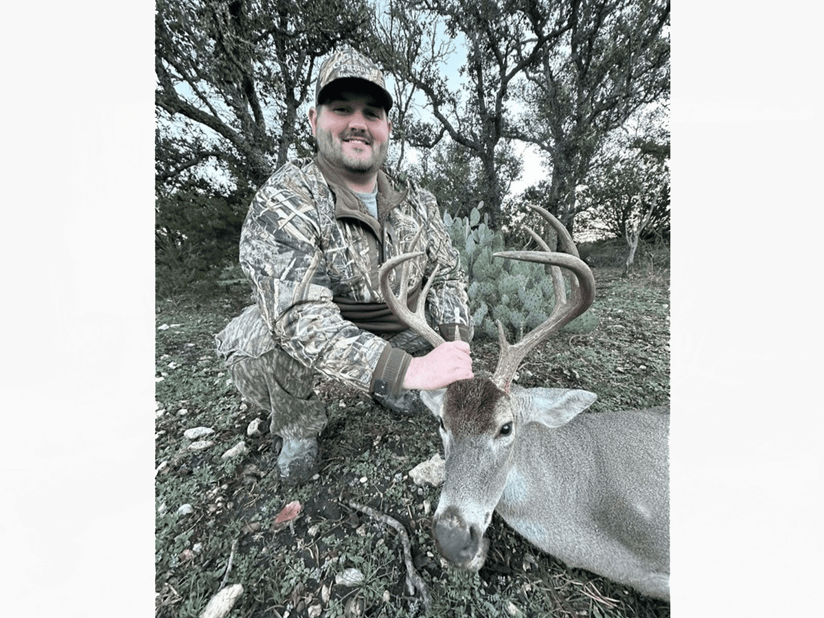Hunter holding a whitetail buck's antlers beside cedar trees