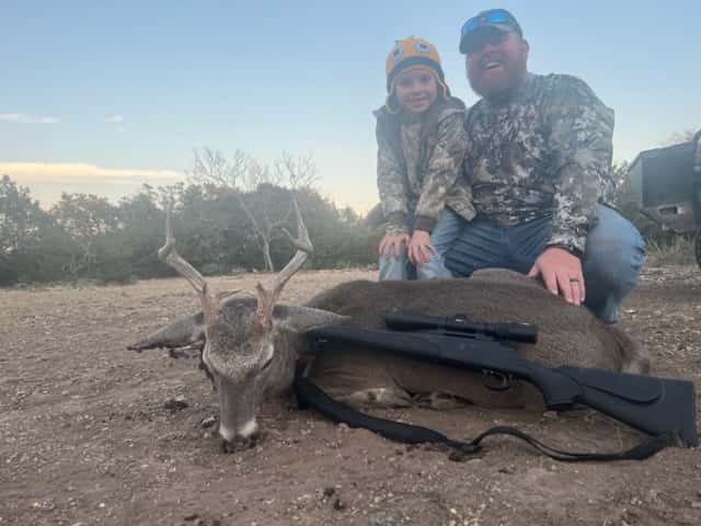 Two hunters with a whitetail buck and rifle in a clearing