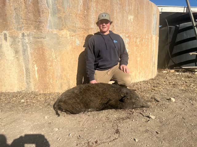 Hunter with a harvested hog beside a round tank