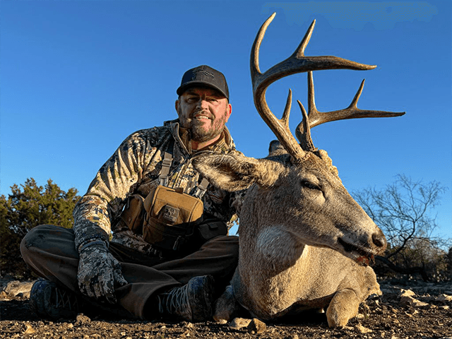 Hunter with a whitetail buck beneath a clear blue sky