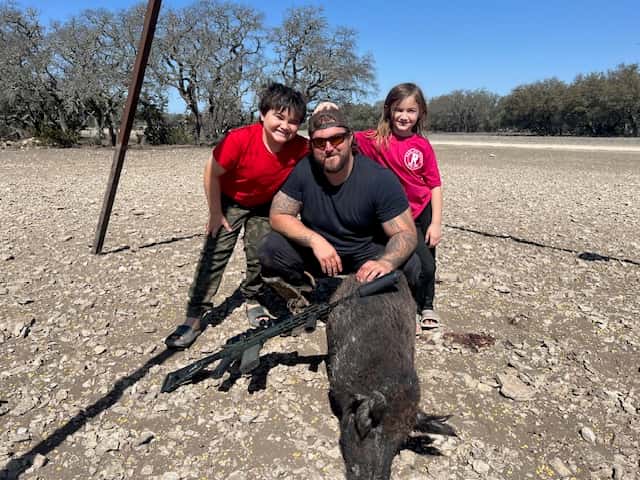 Three hunters with a harvested hog in a sunny clearing