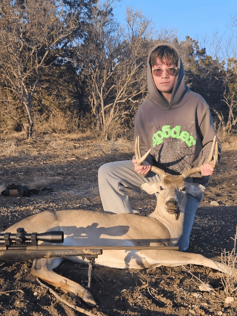 Hunter seated behind a whitetail buck with a rifle in the foreground