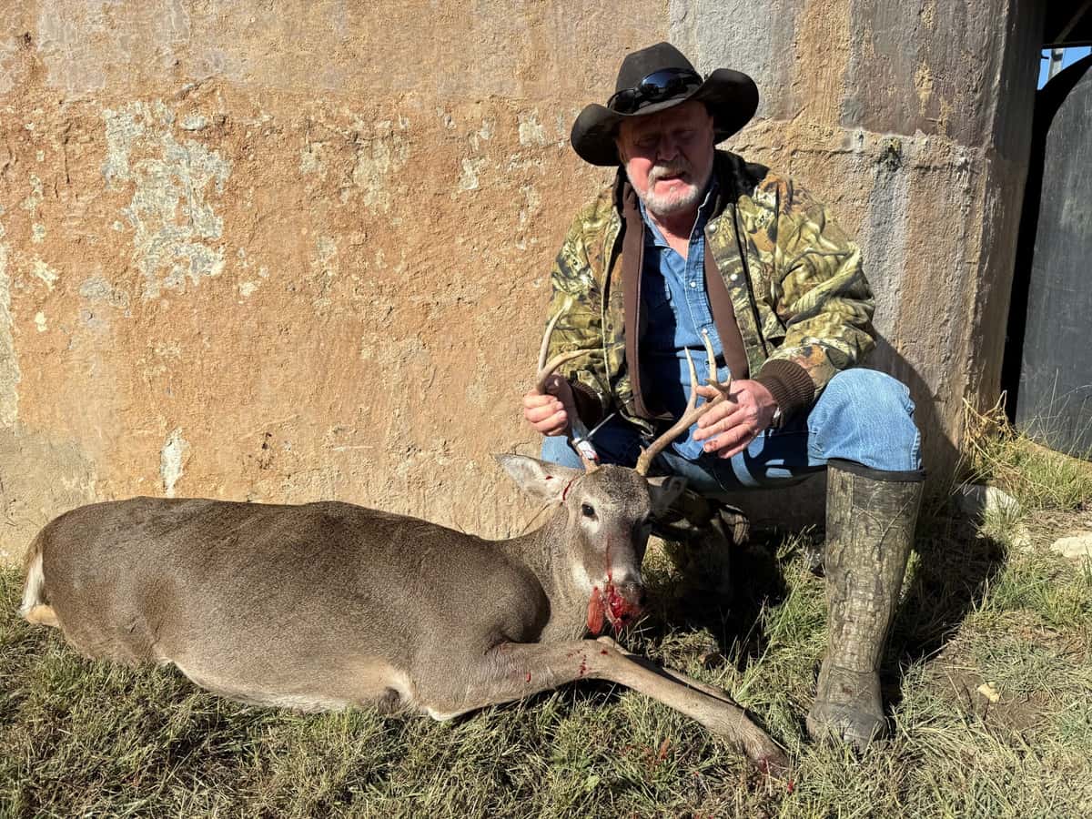 Hunter in a black hat with a whitetail buck beside a tank